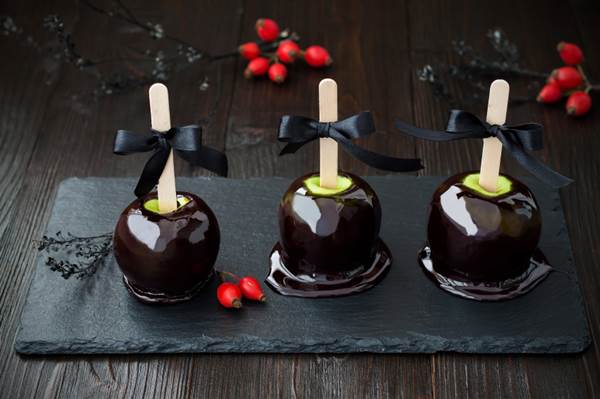 Three black poison caramel apples. Traditional dessert recipe for Halloween party. Selective focus.