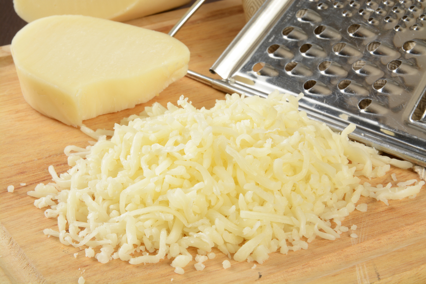 Shredded mozzarella cheese on a cutting board with a grater