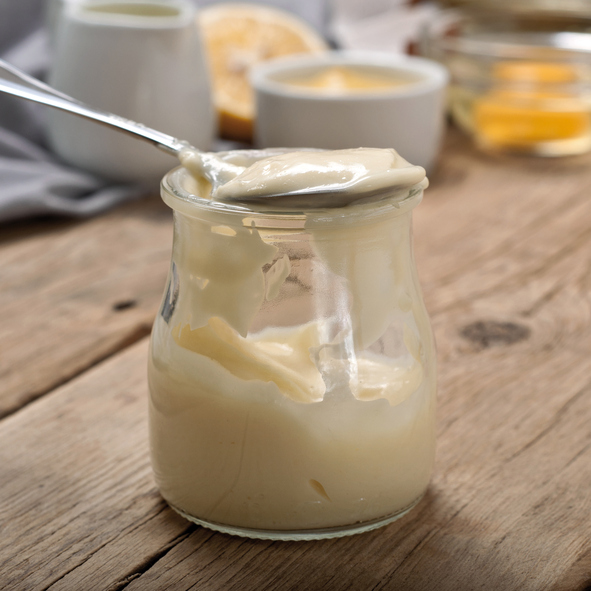 Homemade mayonnaise in glass jar closeup on a wooden table. Square frame